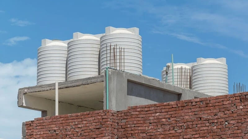 پنج مخزن آب پلاستیکی در بالای پشتم بام یک ساختمان نیمه ساز