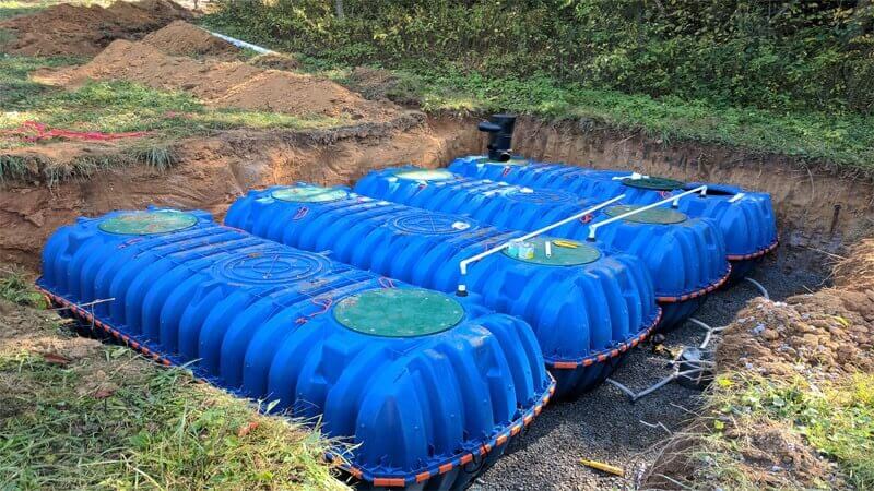 چهار مخزن آب با رنگ آبی که در نزیدیکی مزرعه کشاورزی در گودالی قرار دارند و آماده دفن می‌باشند